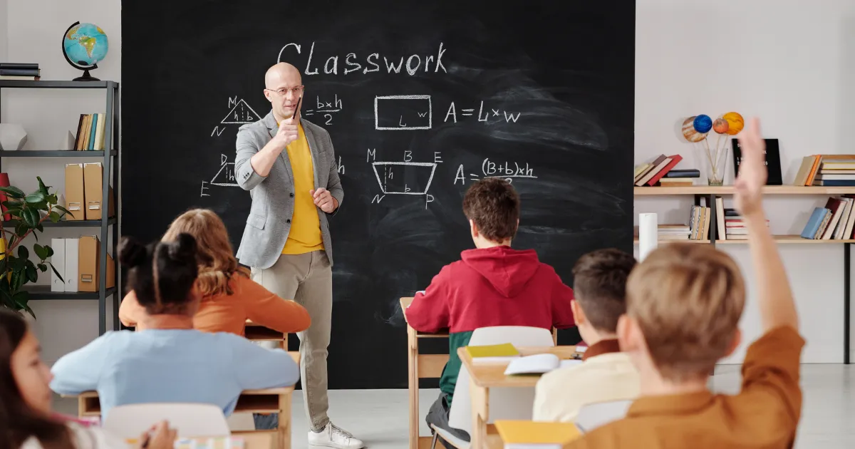Učiteľ stojí pred tabuľou pred žiakmi.