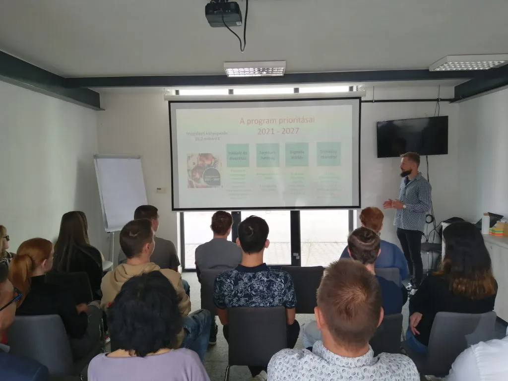 Na fotke prezentuje muž v učebni pred poslucháčmi.