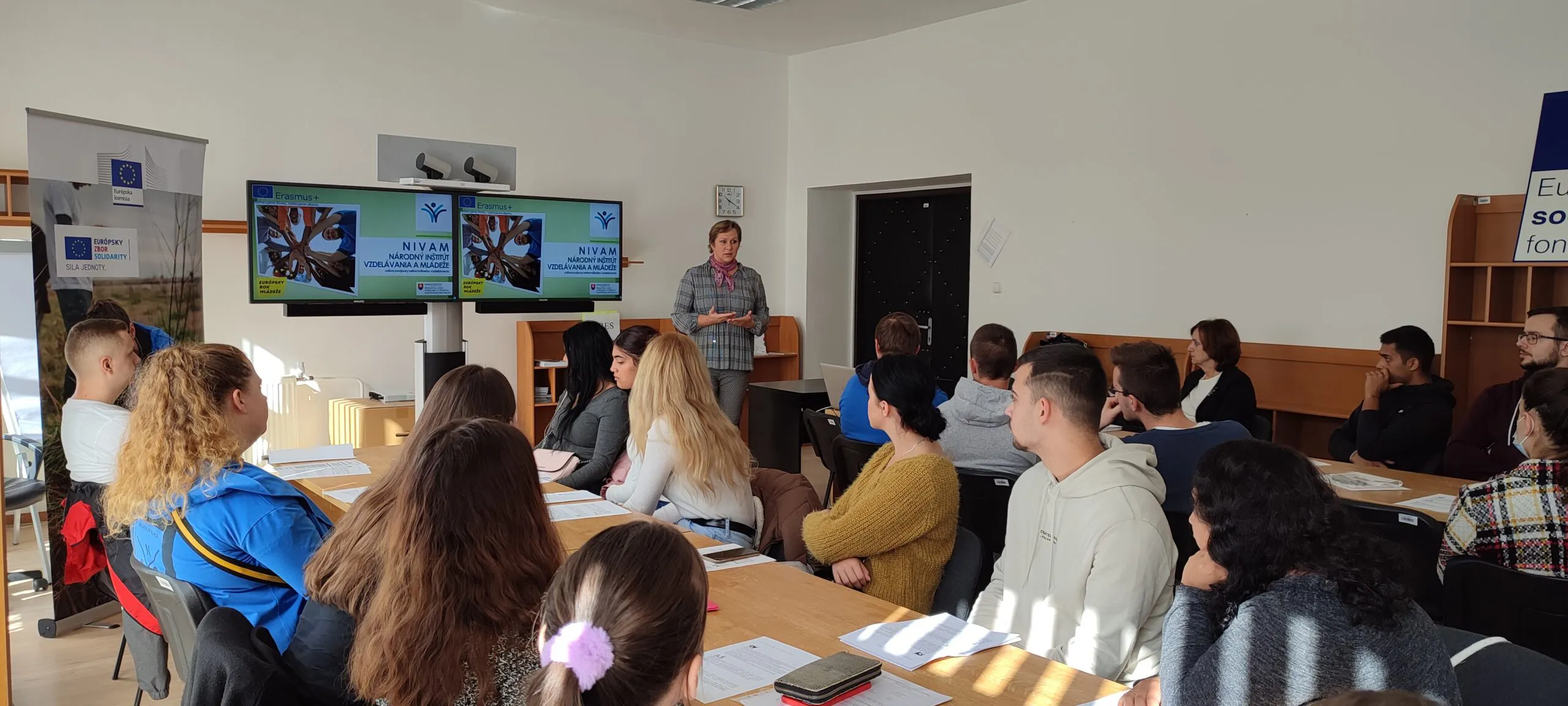Na fotke prezentuje žena v učebni pred poslucháčmi.