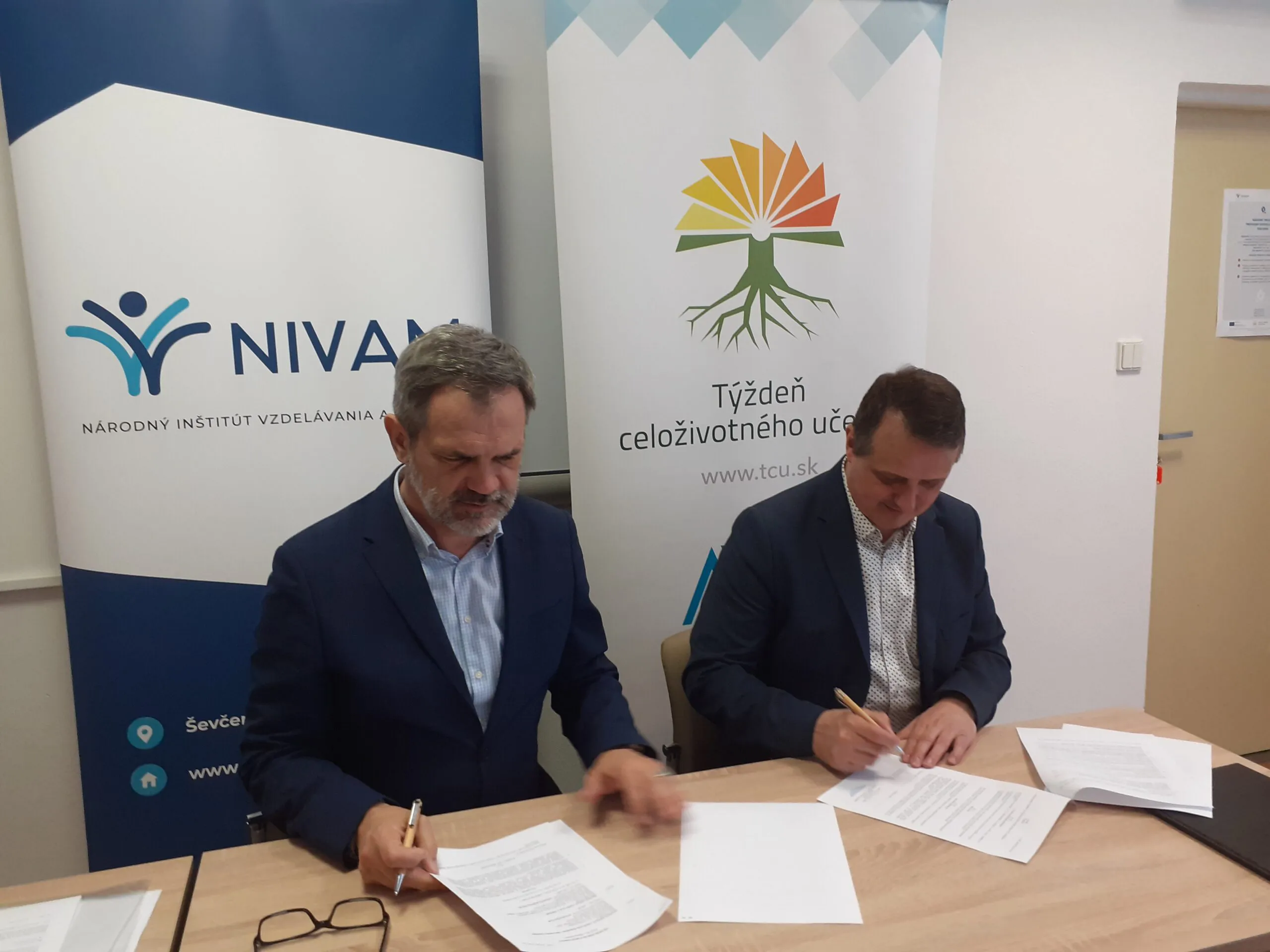 Záber na dvoch mužov, ktorí majú pred sebou papiere.