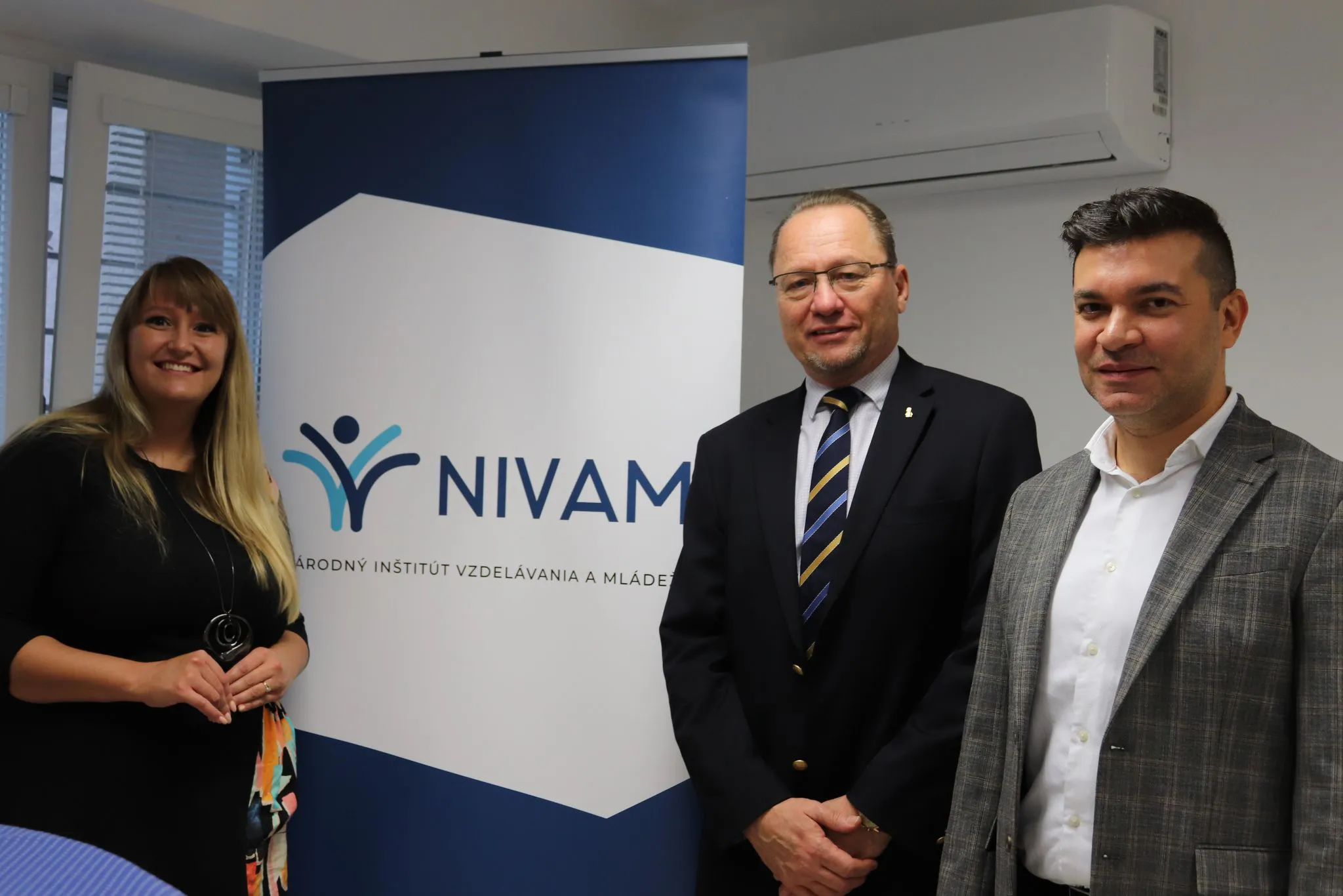 Osoby stoja pri banneri NIVAM.