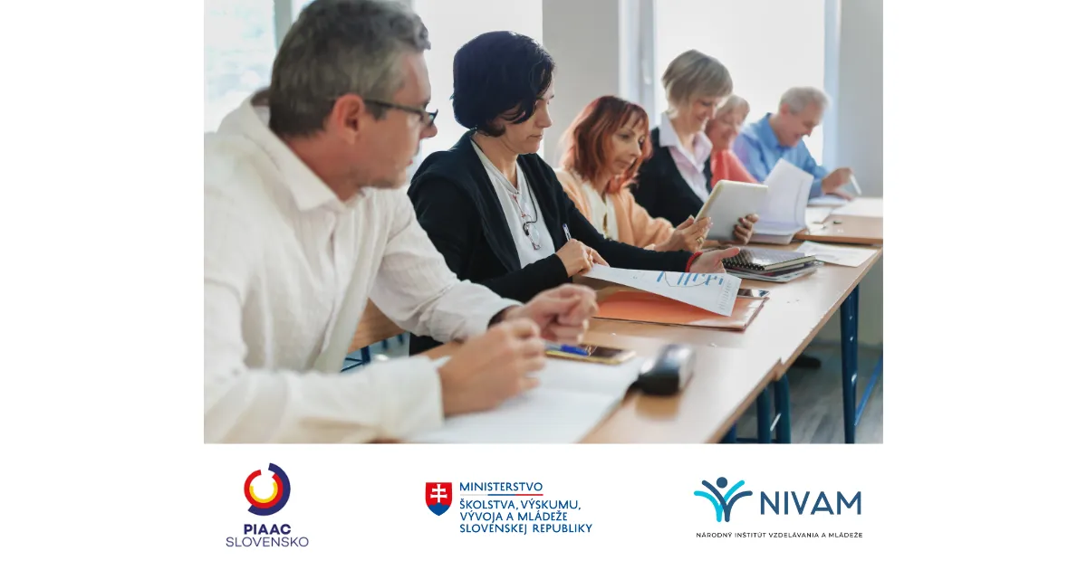 Učiteľka stojí s úsmevom pre školskou katedrou.