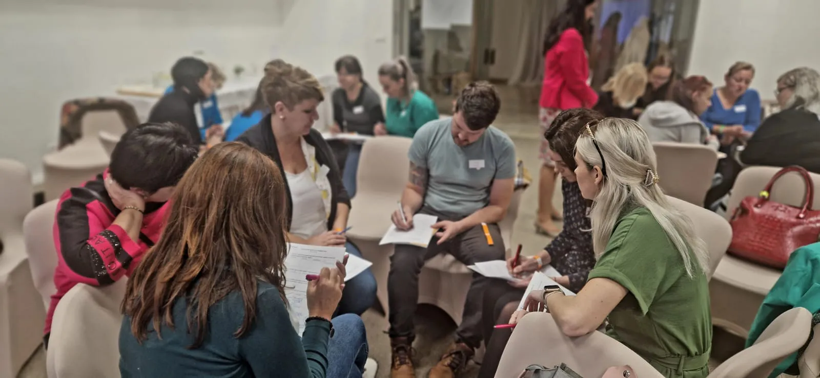 Fotka z podujatia - učitelia sedia v kruhu a píšu na papier poznámky.